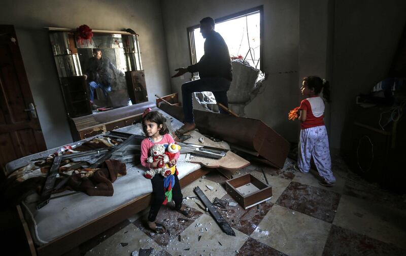 Young girls and a man gather among debris and shattered glass in a room that was hit during an Israeli air strike. AFP