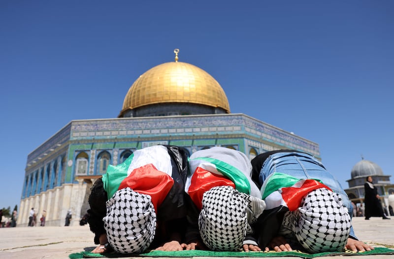 Palestinian men wearing national flags kneel to pray near the Dome of the Rock shrine in the Al Aqsa Mosque compound. AFP