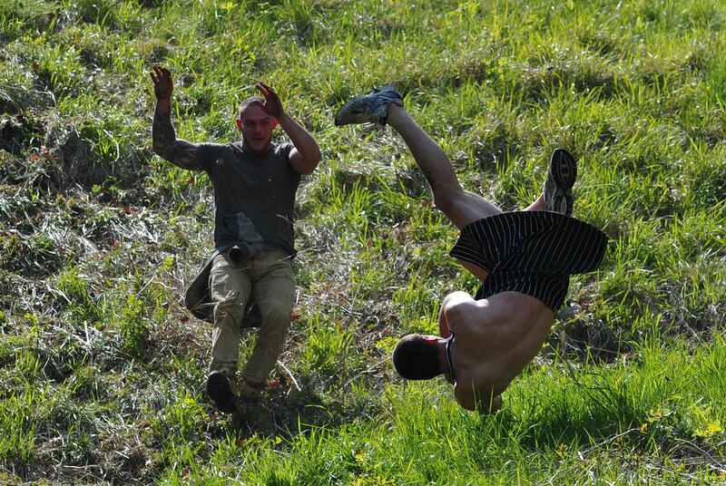 A competitor tumbles down Coopers Hill in pursuit of a fake foam round Double Gloucester cheese during the annual cheese rolling and wake near the village of Brockworth near Gloucester in western England on May 27, 2013. With a disputed history dating back to at least the 1800s, the annual Cooper's Hill Cheese Rolling involves hordes of fearless competitors chasing an eight pound Double Gloucester cheese down a steep hill. The slope has a gradient in places of 1-in-2 and in others 1-in-1, its surface is very rough and uneven and it is almost impossible to remain on foot for the descent. The winner of the race down the hill wins the cheese. AFP PHOTO/CARL COURT
 *** Local Caption ***  209877-01-08.jpg