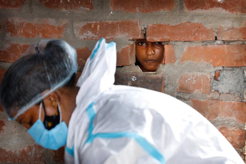 A girl looks out through a hole in the wall of her house as a health worker prepares to carry out Covid-19 testing in Jamsoti village in the Indian state of Uttar Pradesh. AP