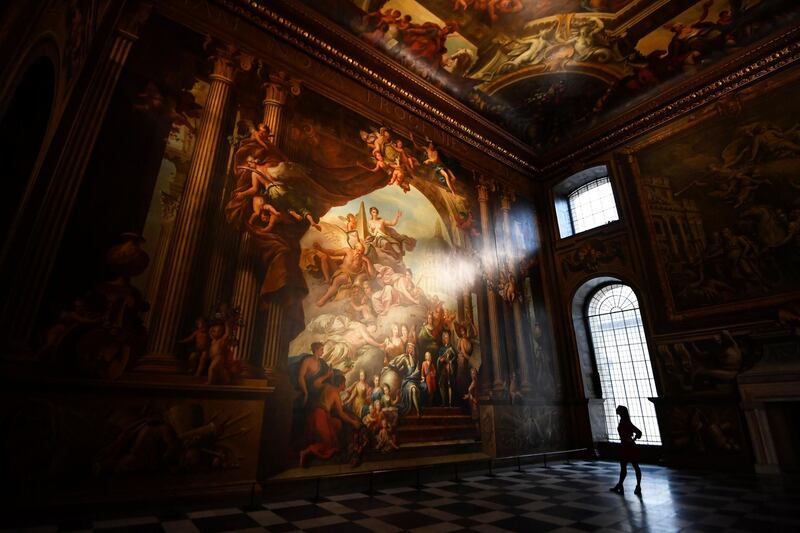 A gallery assistant poses beside a fresco during the reopening of The Painted Hall, Old Royal Navy College in London. Reuters