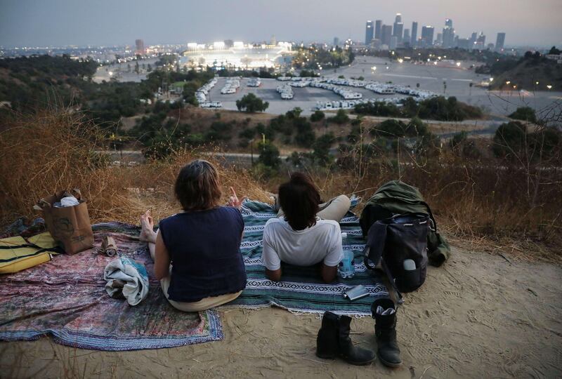 People attempt to watch a game between the Colorado Rockies and the Los Angeles Dodgers from a hillside overlooking Dodger Stadium, while listening to the game broadcast from a mobile phone in Los Angeles, California. Spectators are currently not allowed to attend Major League Baseball games.   AFP
