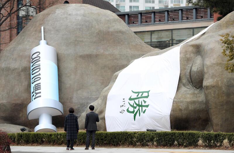 People look at a giant mock syringe for Covid-19 vaccines and a Chinese character meaning 'triumph' in the southeastern city of Daegu, South Korea. EPA