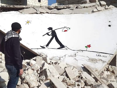Abu Malek Al Shami stands in front of one of his murals painted on the collapsed roof of a building in Idlib, Syria. Abd Almajed Alkarh for The National. 