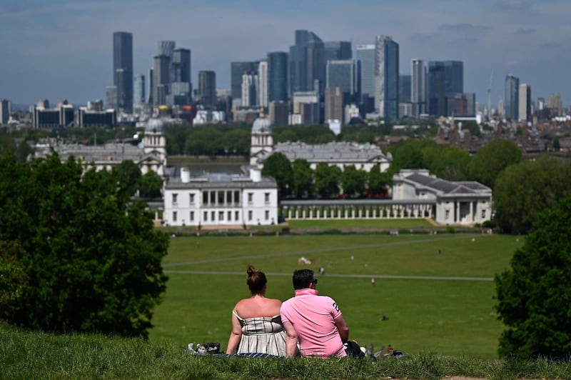 People look at the City of London skyline as they enjoy the warm weather in Greenwich Park, south east London on June 3, 2021. Much of Britain has enjoyed several days of fine weather with top temperatures reaching above 25 degrees Celsius. / AFP / JUSTIN TALLIS
