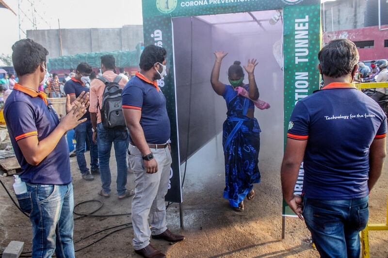 A woman (2R) gestures as she walks through a disinfection tunnel set up at the entrance of Thennampalayam market in Tiruppur district of Tamil Nadu state.  AFP