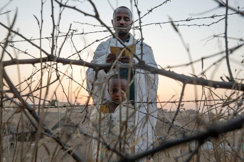 An Orthodox Christian Tigrayan refugee, who fled the conflict in the Ethiopia's Tigray region, reads prayers with his son in front of a church at the Hamdeyat Transition Center, near the Sudan-Ethiopia border, eastern Sudan. AP Photo