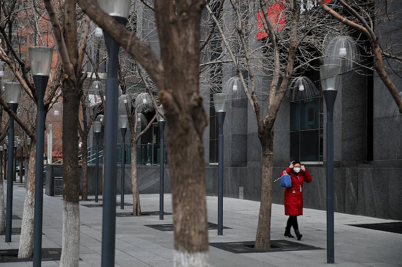 A woman adjusts her protective face mask walks by an office building at the Central Business District in Beijing, Monday, March 2, 2020. China's manufacturing plunged in February as anti-virus controls shut down much of the world's second-largest economy, but companies are confident activity will revive following government stimulus efforts, according to two surveys. (AP Photo/Andy Wong)