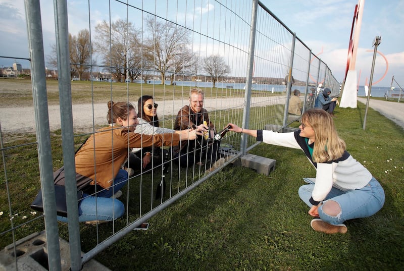 Friends clink with beer bottles through a fence built by German authorities on the German-Swiss border, as a protection measure due to the spread of the coronavirus disease (COVID-19), in an park on the banks of Lake Constance in Kreuzlingen, Switzerland. REUTERS