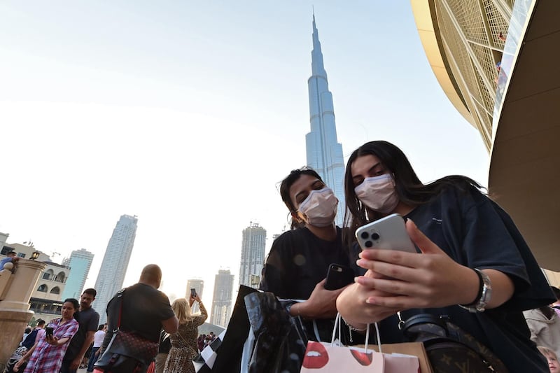 Women wearing protective masks pose for a "selfie" picture on a cell phone in front of Burj Khalifa, the tallest structure and building in the world since 2009 (total heigh with antenna of 829.8 metres), in the city centre of the Gulf emirate of Dubai on March 8, 2020.  / AFP / GIUSEPPE CACACE

