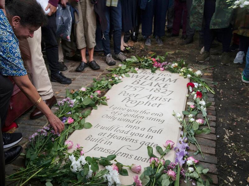 A woman lays a flower as people gather around a newly unveiled headstone for English poet William Blake at Bunhill Fields in London after it is unveiled, Sunday Aug. 12, 2018. The lost grave of William Blake is marked with a new gravestone, nearly two centuries after the poet and painter was buried in an unmarked common grave in Bunhill Fields. There was a plain memorial stone in the cemetery that simply recorded that the artist was buried nearby, but the exact site of Blake's grave was lost to history until it was re-discovered by two members of the Blake Society in 2006. (Victoria Jones/PA via AP)