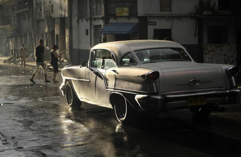 People cross a street as a U.S.-made car, used as a private collective taxi is driven as it rains in Havana September 30, 2013. Collective taxis, also known as "almendron" (big nutshell), have established routes around or near Havana, picking up and dropping off passengers along the way. The price of a journey in these taxis ranges from $0.50 for a ride within the city to $1 for a 30km (18.7 mile) ride to the outskirts of Havana. REUTERS/Desmond Boylan (CUBA - Tags: TRANSPORT BUSINESS EMPLOYMENT ENVIRONMENT) *** Local Caption ***  HAV03_CUBA-_1001_11.JPG