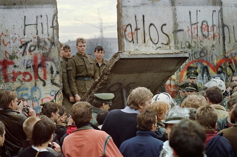 (FILES) This file photo taken on November 11, 1989 shows West Berliners who are crowded in front of the Berlin Wall early 11 November 1989 as they watch East German border guards demolishing a section of the wall in order to open a new crossing point between East and West Berlin, near the Potsdamer Square. The Iron Curtain was at first an ideological and then a physical separation of communist Eastern Europe from the West from the 1940s after World War II. / AFP / GERARD MALIE
