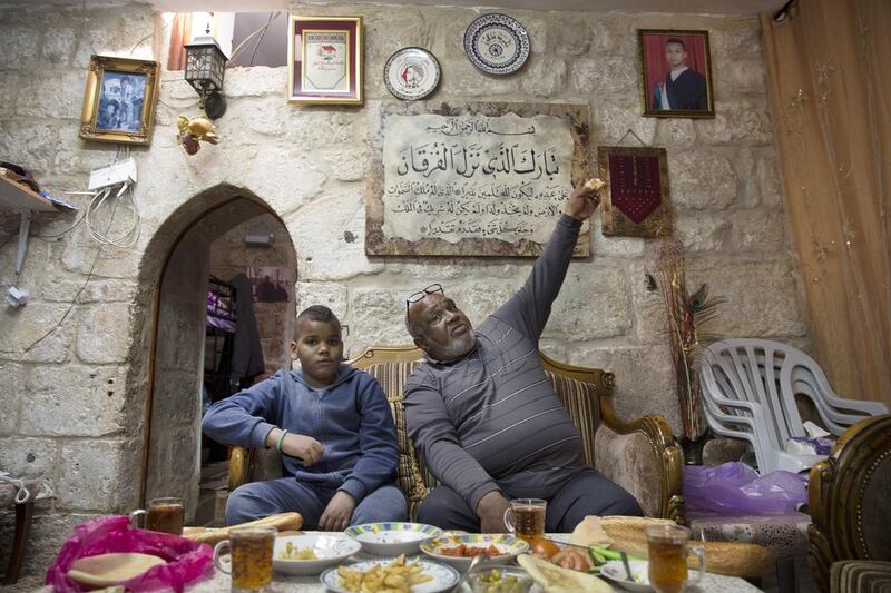 Afro-Palestinian Shahlin Husani having lunch with Muron, his son, after a Friday prayer this month. Mr Husani points to a photograph of a relative, Ossama Jebdeh, who he claims was one of the first Palestinians to be killed during the second uprising.  Heidi Levine for The National