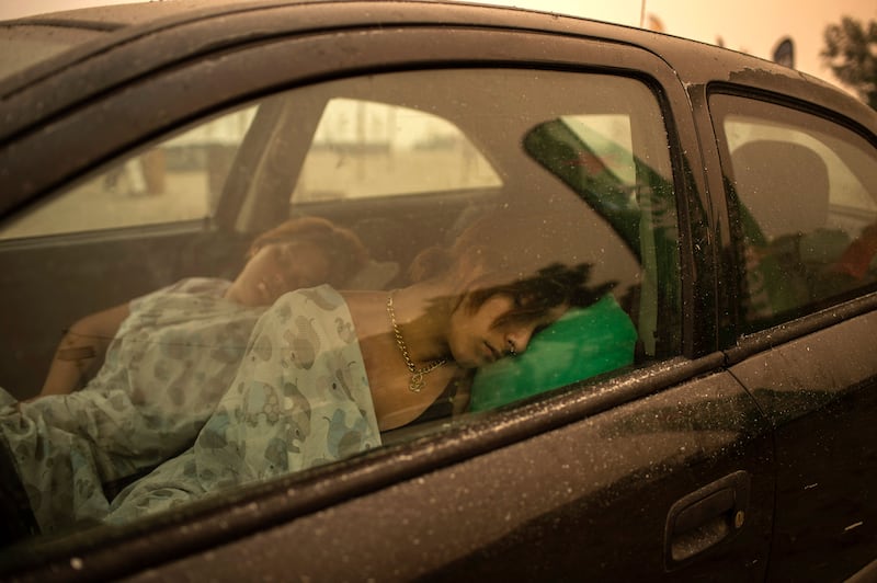 A woman and a child sleep in a car on the beach as wildfires rage in Pefki.