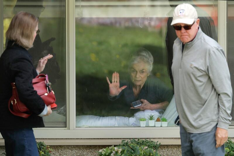 Judie Shape, centre, who has tested positive for the coronavirus, but isn't showing symptoms, presses her hand against her window after a visit through the window and on the phone with her daughter Lori Spencer, left, and her son-in-law Michael Spencer, at the Life Care Center in Kirkland. AP Photo