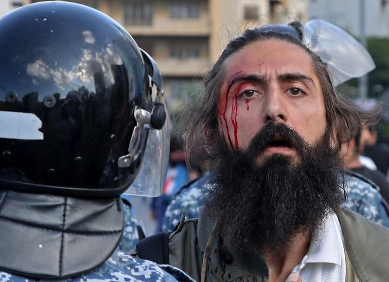 An injured man stands near Lebanese security forces trying to prevent clashes between demonstrators and counter-protesters in the centre of the capital Beirut during the 13th day of anti-government protests. AFP