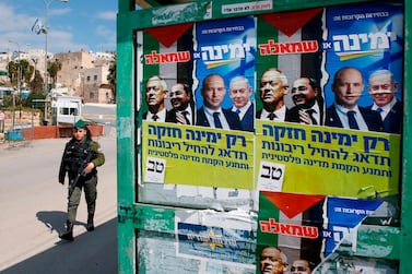 A member of the Israeli security forces walks past election posters of Israel's Blue and White political alliance leader Benny Gantz, Arab Israeli member of the Joint List Ahmad Tibi, Isreali Defense Minister Naftali Bennett and Prime Minister Benjamin Netanyahu in the divided West Bank town of Hebron. AFP