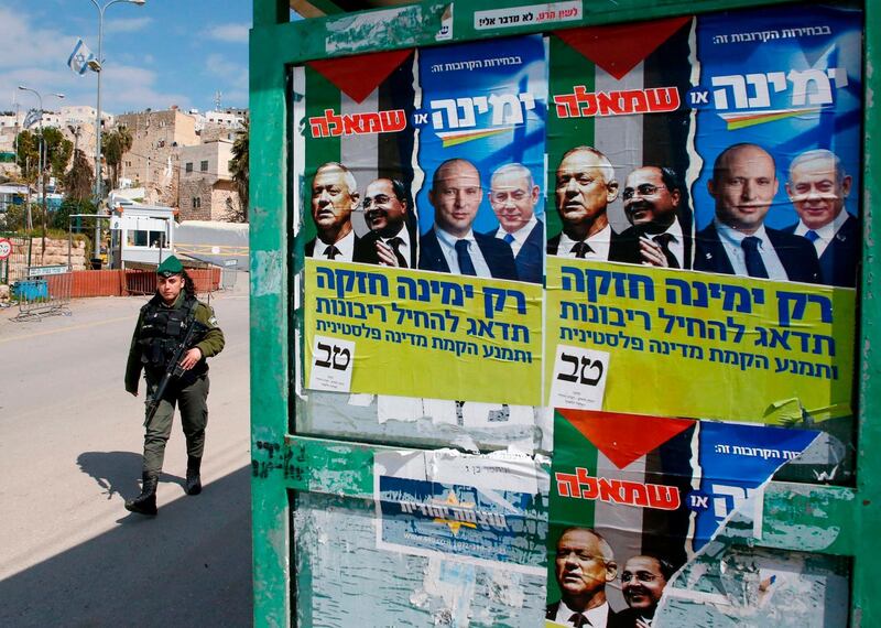 A member of the Israeli security forces walks past election posters of Israel's Blue and White political alliance leader (Kahol Lavan) Benny Gantz, Arab Israeli member of the Joint List Ahmad Tibi, Isreali Defense Minister Naftali Bennett and Prime Minister Benjamin Netanyahu, near the Ibrahimi mosque, also known to Jews as the Cave of the Patriarchs, in the divided West Bank town of Hebron on February 23, 2020.  / AFP / HAZEM BADER
