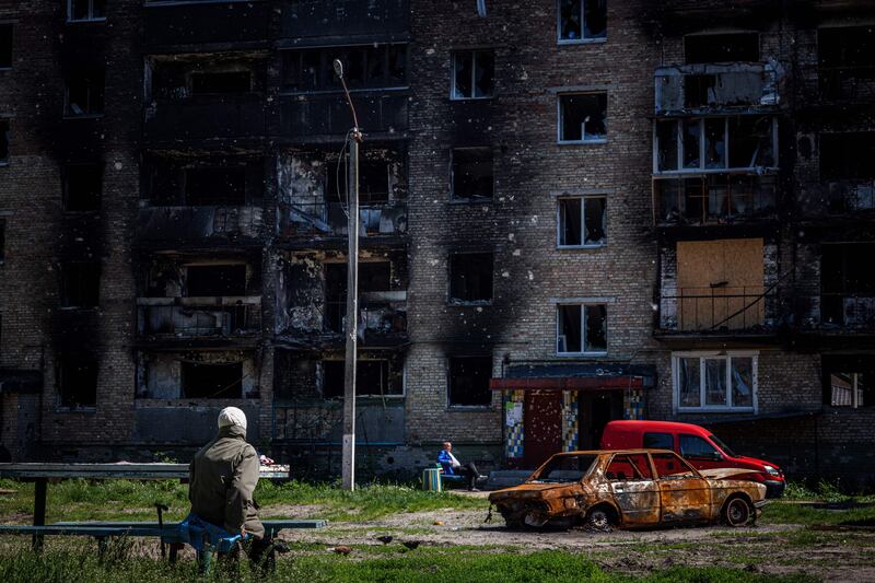 People sit next to a damaged apartment building in Irpin, near Kyiv. AFP