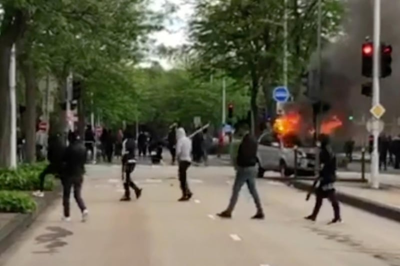 This frame grab provided by BFM TV shows youths, some holding sticks, walking by a burning car in Dijon, central France, Monday June 15, 2020. The French government sent police reinforcements and a top official to the Dijon region to quell four nights of unusually violent clashes between rival groups that have left at least 10 injured and cars burned and rattled the community. The reasons for the violence are under investigation, but local officials say it appears linked to the drug trade and tensions between members of France's Chechen community and other groups. (BFM TV via AP)