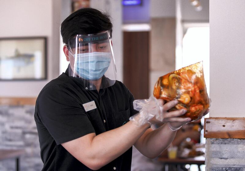 Abu Dhabi, United Arab Emirates, July 4, 2020.   
  A waiter from Off The Hook Seafood Restaurant serves a bag of seafood goodness at the Tourist Club Area, Abu Dhabi.
Victor Besa  / The National
Section:  NA 
Reporter: