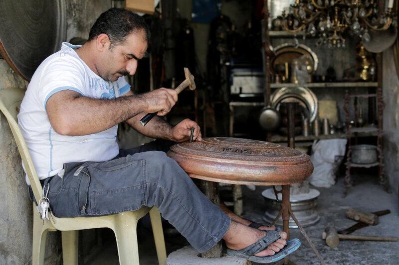 In this Sunday, July 28, 2019 photo, Ahmad Zuhdi Ghazoul works on a piece of copper on the newly renovated copper market in Aleppo, Syria. Much of Aleppo's centuries-old covered market is still in ruins but slowly small parts of it have been renovated where business is slowly coming back to normal nearly three years after major battles in Syria's largest city and once commercial center came to an end. (AP Photo/Hassan Ammar)