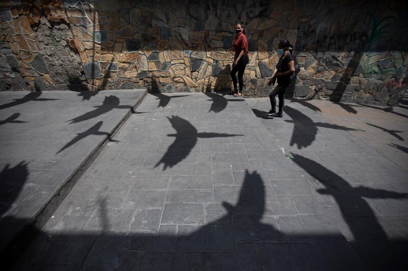 The shadows of synthetic macaws are cast on the pavement as pedestrians wearing protective face masks walk past, in the Petare neighborhood of Caracas, Venezuela.  AP