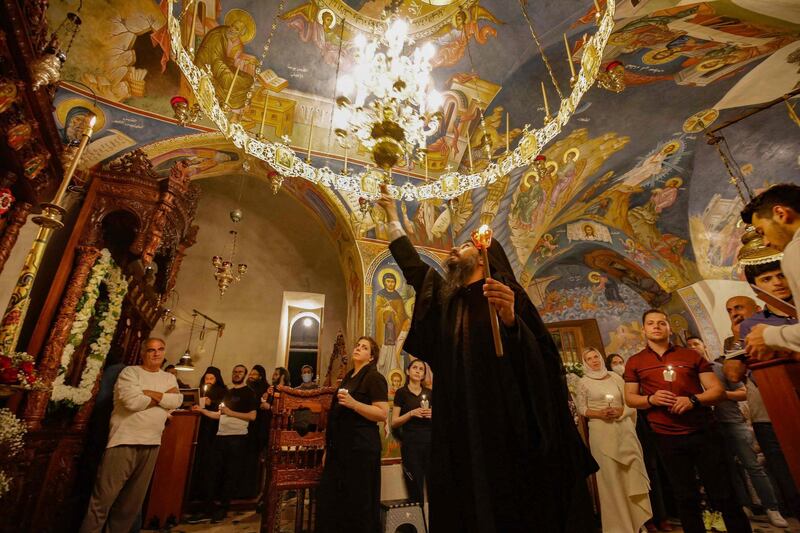 People gather as a Greek Orthodox priest adjusts a chandelier during the Easter night Mass at the ancient monastery of Our Lady of Hamatoura, built in the rocky hollow of a high cliff in the town of Karm Sadde which overlooks the holy valley of Qadisha, north of Beirut. AFP