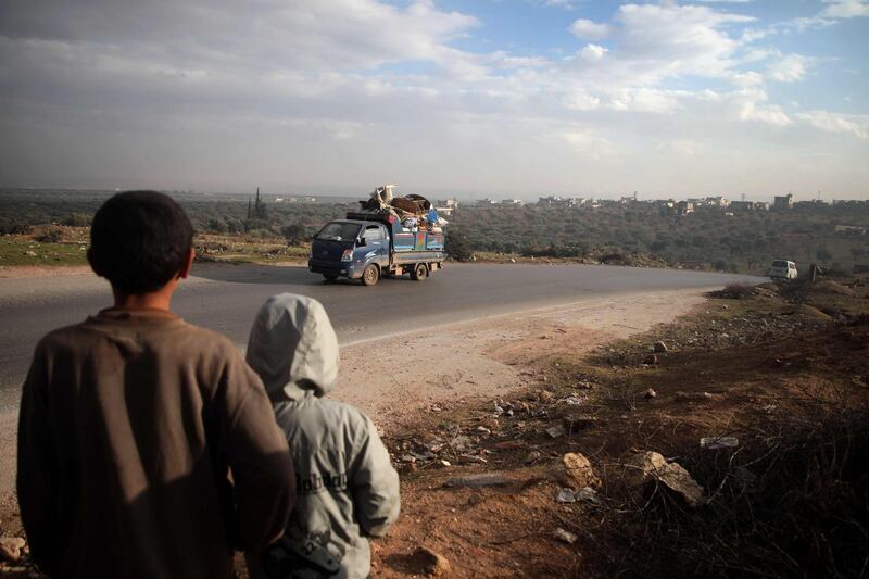 TOPSHOT - Boys look on at a truck loaded with furniture and belongings as in the village of al-Mastumah, about seven kilometres south of the city of Idlib on December 24, 2019, as Syrian families from the south of Idlib province drive through towards the Syrian-Turkish border fleeing the assault led by government forces and their allies.  / AFP / Aaref WATAD
