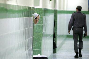 An inmate peers from behind a wall as a guard walks by, at the female section of Evin jail, north of Tehran, 13 June 2006. AFP