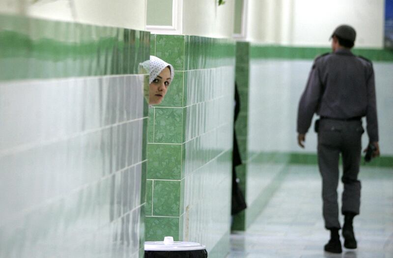 TO GO WITH AFP STORY IRAN-JUSTICE-PRISON-SOCIT BY PIERRE CELERIER 
An Iranian inmate peers from behind a wall as a guard walks by at the female section of the infamous Evin jail, north of Tehran, 13 June 2006. AFP PHOTO/ATTA KENARE (Photo by ATTA KENARE / AFP)