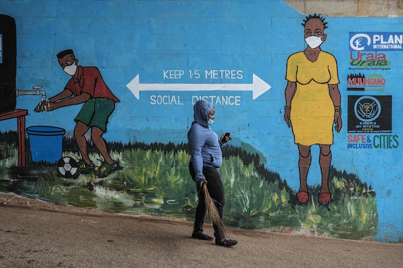 A woman wearing a face mask walks past graffiti that promotes social distancing amid the ongoing coronavirus pandemic, in Kibera, Nairobi.  AFP