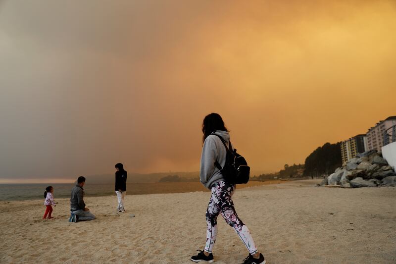 People visit the beach as a forest fire burns 