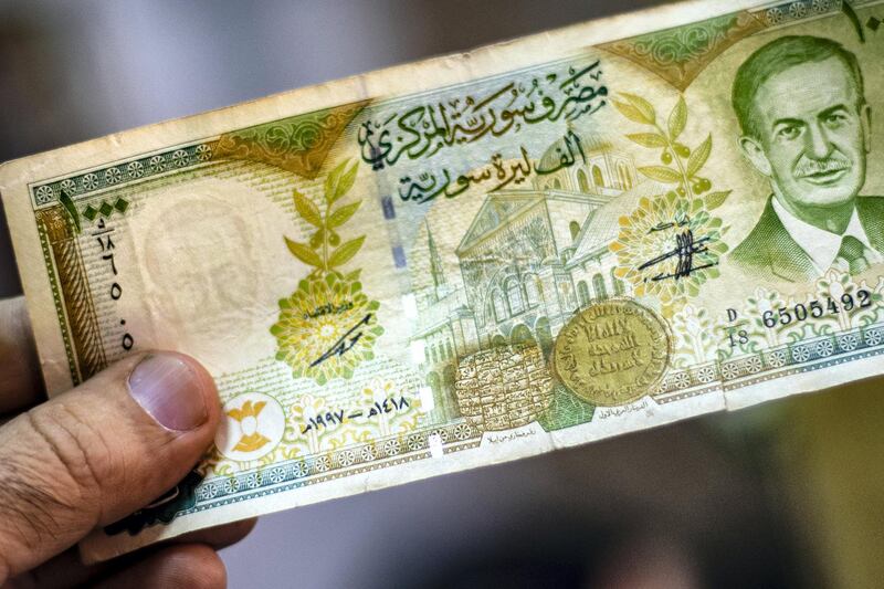 A merchant holds a Syrian pound note, bearing a portrait of late Syrian President Hafez al-Assad, at a market in the Kurdish-majority city of Qamishli in northeast Syria on September 10, 2019. - The declining value of the pound is a sure sign of Syria's ailing economy. 
The civil war has battered the country's finances and depleted its foreign reserves. 
A flurry of international sanctions on President Bashar al-Assad's regime and associated businessmen since the start of the war in 2011 has compounded the situation. (Photo by Delil SOULEIMAN / AFP)