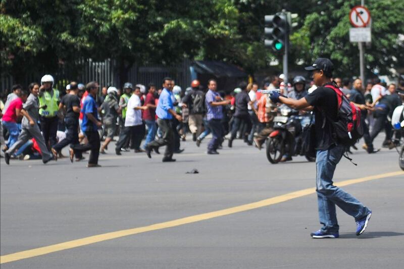 An unidentified man with a gun walks in the street as people run in the background on Thamrin street near Sarinah shopping mall in Jakarta, Indonesia. Veri Sanovri / Xinhua via AP