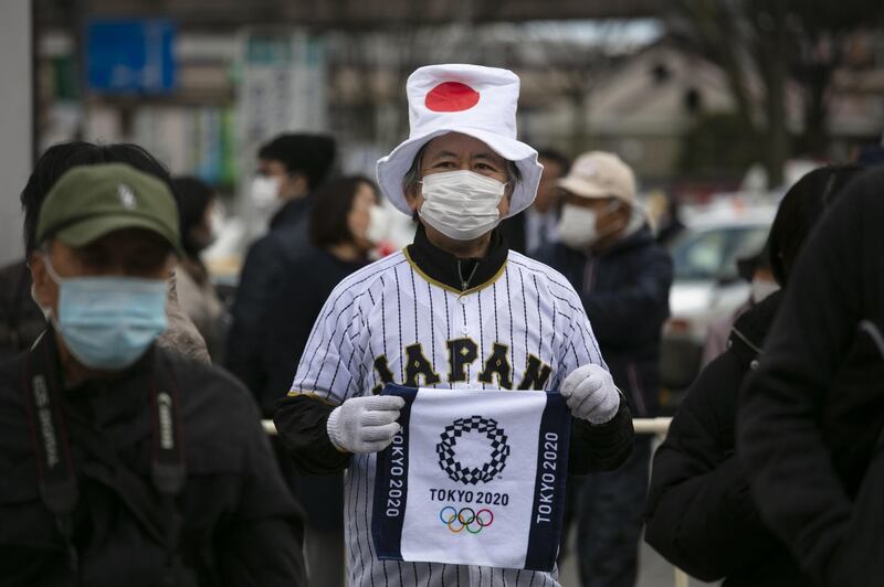 A man wearing a Japanese flag-themed hat shows a towel with a Tokyo 2020 Olympics logo printed on while waiting in line to view the Olympic Flame in Fukushima City, Japan. AP