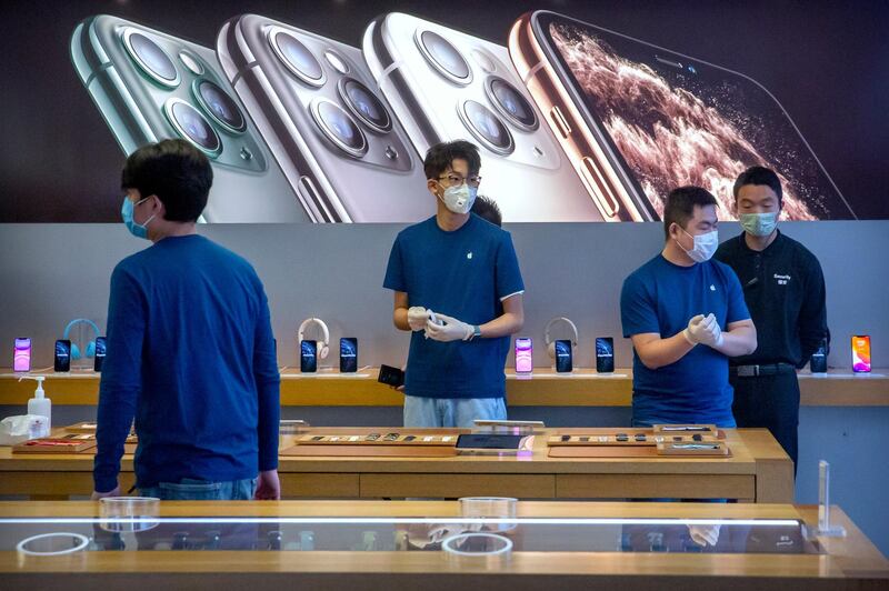 FILE - In a Feb. 14, 2020 file photo, employees wear face masks as they stand in a reopened Apple Store in Beijing. Apple Inc. is warning investors that it won't meet its second-quarter financial guidance because the viral outbreak in China has cut production of iPhones. The Cupertino, California-based company said Monday, Feb. 17, 2020 that all of its iPhone manufacturing facilities are outside Hubei province, and all have been reopened, but production is ramping up slowly. (AP Photo/Mark Schiefelbein, File)