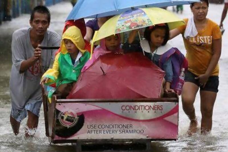 A man pushes a cart full of children as they cross a flooded road in suburban Pasig, east of Manila, yesterday.