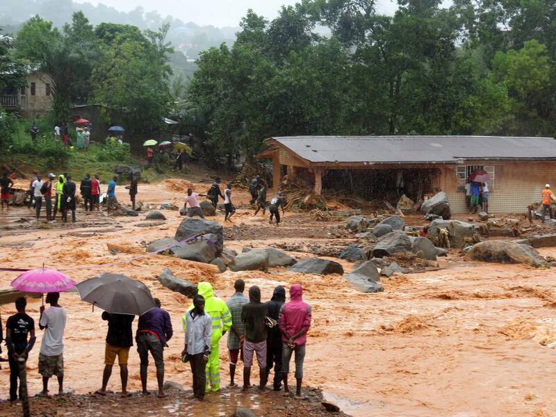 Bystanders look on as floodwaters rage past a damaged building in an area of Freetown on August 14, 2017, after landslides struck the capital of the west African state of Sierra Leone.               
At least 312 people were killed and more than 2,000 left homeless when heavy flooding hit Sierra Leone's capital of Freetown, leaving morgues overflowing and residents desperately searching for loved ones. An AFP journalist at the scene saw bodies being carried away and houses submerged in two areas of the city, where roads turned into churning rivers of mud and corpses were washed up on the streets.
 / AFP PHOTO / SAIDU BAH