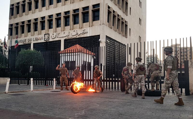 Lebanese Army soldiers roll away a flaming tire from the fence surrounding the local branch of the Banque du Liban (Lebanese Central Bank) as protesters gather to demonstrate against dire economic conditions in the northern city of Tripoli on June 11, 2020. - The Lebanese pound sank to a record low on the black market on June 11 despite the authorities' attempts to halt the plunge of the crisis-hit country's currency, money changers said. Lebanon is in the grips of its worst economic turmoil in decades, and holding talks with the International Monetary Fund towards securing billions in aid to help overcome it. (Photo by Fathi AL-MASRI / AFP)