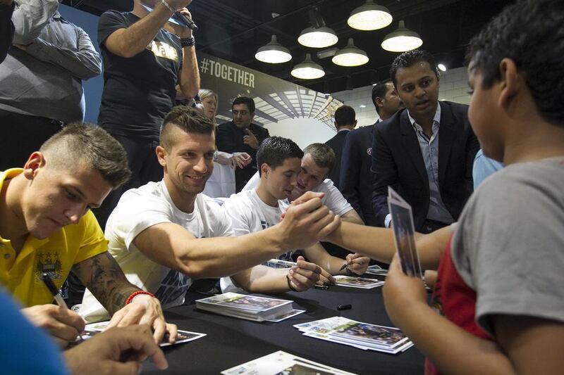 Manchester City player Stevan Jovetic, centre, shakes a young fan's hand while Matija Nastasic, left, and Samir Nasri, right, sign autographs during their appearance at Marina Mall in Abu Dhabi on Tuesday. Mona Al-Marzooqi / The National / May 13, 2014