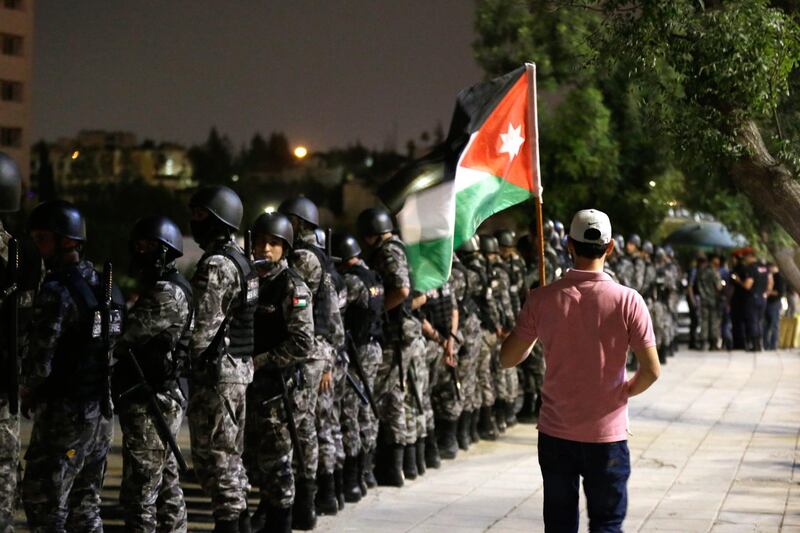 epa06792145 A protester holds a Jordanian national flag as security forces stand guard, during celebrations of the withdrawal of disputed tax reform, in Amman, Jordan, 08 June 2018. Reports state that al-Razzaz met on 06 June 2018 with members of the Parliament also Jordanian professional syndicates representatives and announced that the disputed new tax reform project would be withdrawn and other subjects of disagreement would be re-discussed. He was appointed on 04 June, following a week long protests against his predecessor's reforms. Protesters had taken to the streets to demand the withdrawal of the new taxes, the return to bread subsidy and a change in the country's economic policies.  EPA/ANDRE PAIN