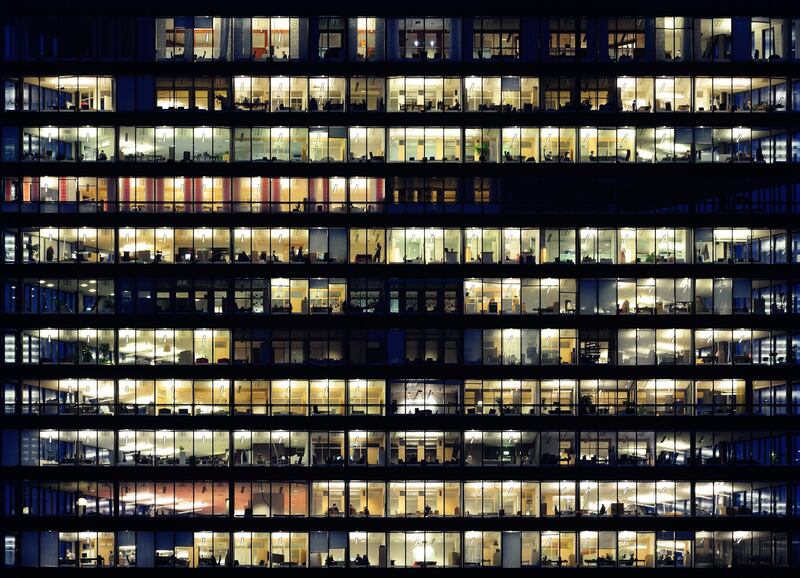 Lots of people working late. Employees seen as silhouettes against their brightly lit offices with large windows. Building lit by the "blue hour" evening sky. Getty Images