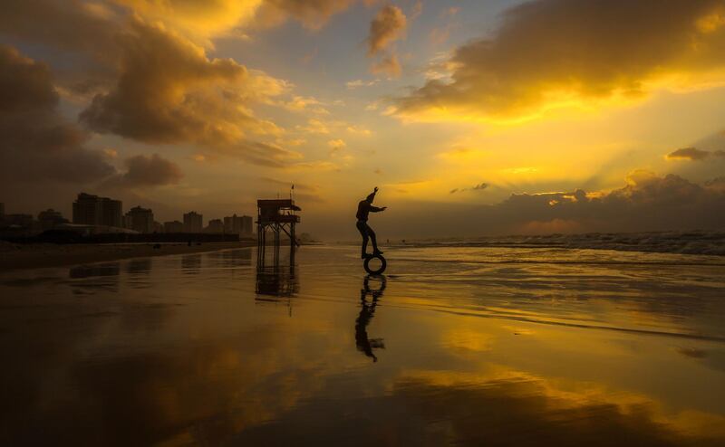 A Palestinian youth attempts to balance on a tire on the beach at sunset in Gaza City. Mahmud Hams / AFP Photo.