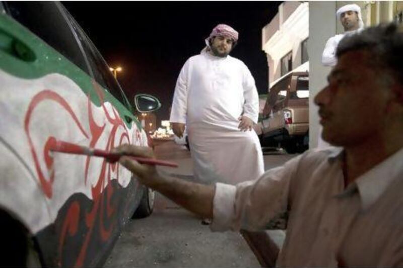 Ali Abdullatef of Abu Dhabi watches as an Emirates Arts employee paints his car for the National Day celebrations in Ras al Khaimah.