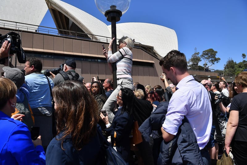 A royal fan climbs a lamppost to get a glimpse of Prince Harry and Meghan as they conduct a meet the people walk at the Sydney Opera House. EPA
