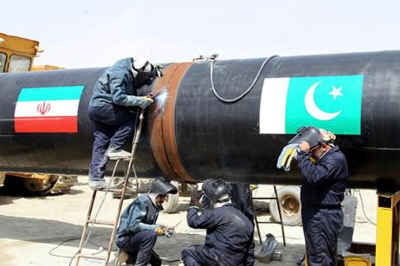Iranians work on a section of a pipeline (on with are sticked Iranian and Pakistanese national flags) after the project was launched during a ceremony with presidents of Iran and Pakistan on March 11, 2013 in the Iranian border city of Chah Bahar. The two leaders jointly unveiled a plaque before shaking hands and offering prayers for the successful conclusion of the project, which involves the laying of a 780 kilometre (485 mile) section of the pipeline on the Pakistani side, expected to cost some $1.5 billion.  AFP PHOTO/ATTA KENARE