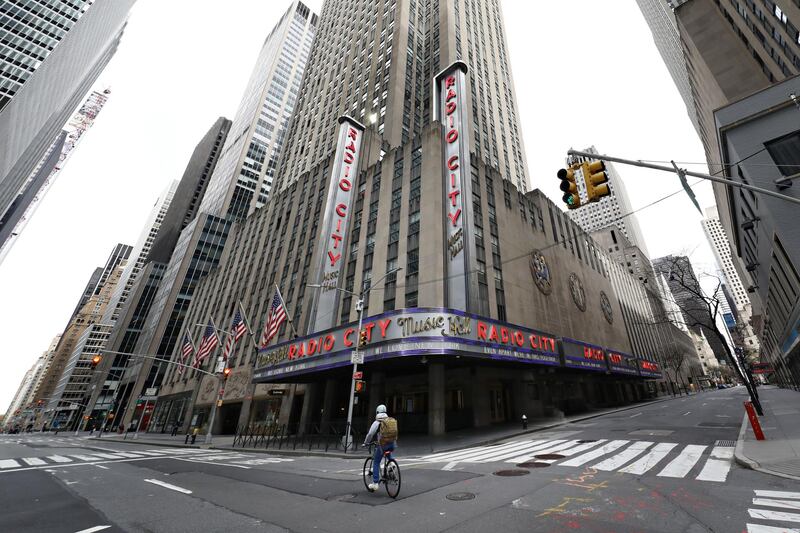 NEW YORK, NEW YORK - APRIL 20: A person on a bicycle rides in front of Radio City Music Hall during the coronavirus pandemic on April 20, 2020 in New York City. COVID-19 has spread to most countries around the world, claiming more than 170,000 lives with over 2.4 million infections reported.   Cindy Ord/Getty Images/AFP