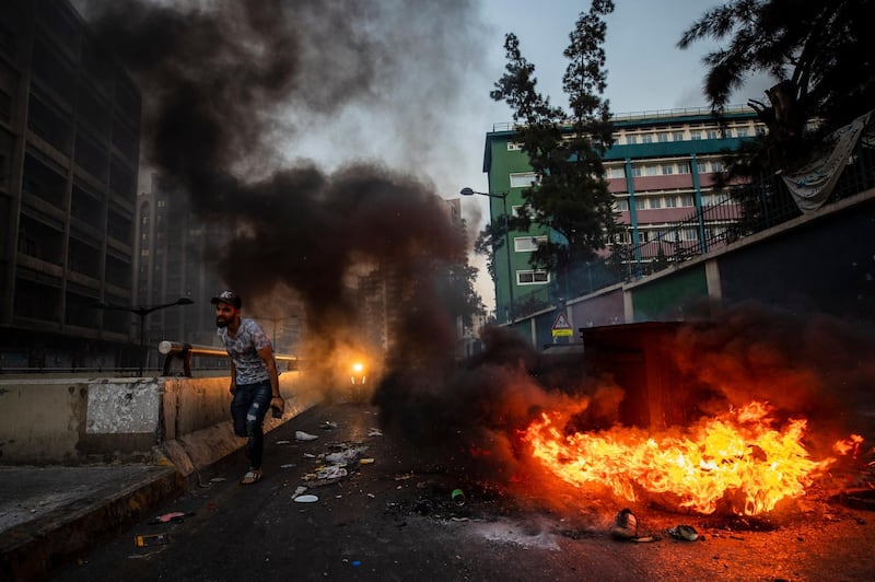 People pass garbage containers and tires that were set on fire by anti-government protesters to block the main road in Beirut, Lebanon. AP Photo